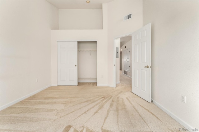 unfurnished bedroom featuring a closet, light colored carpet, and a high ceiling