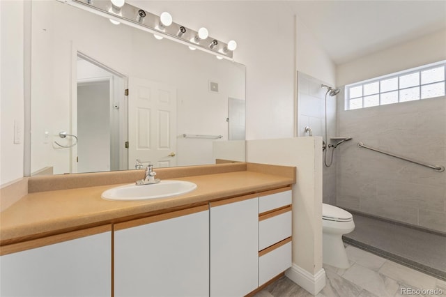 bathroom with a tile shower, vanity, and toilet