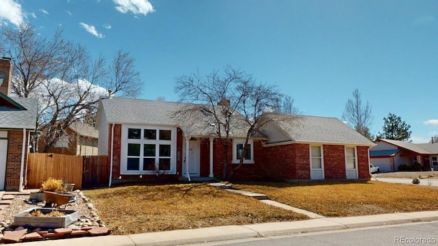 single story home featuring brick siding, a front lawn, a shingled roof, and fence