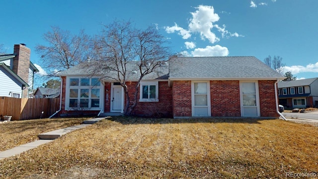 ranch-style house with a shingled roof, brick siding, fence, and a front lawn