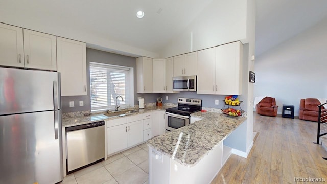 kitchen with light stone counters, stainless steel appliances, a peninsula, a sink, and white cabinets