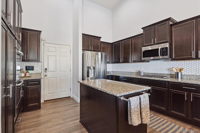 kitchen with appliances with stainless steel finishes, a towering ceiling, light hardwood / wood-style floors, and dark brown cabinetry