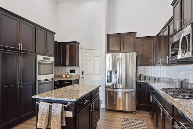 kitchen featuring a center island, a towering ceiling, stainless steel appliances, and light stone counters