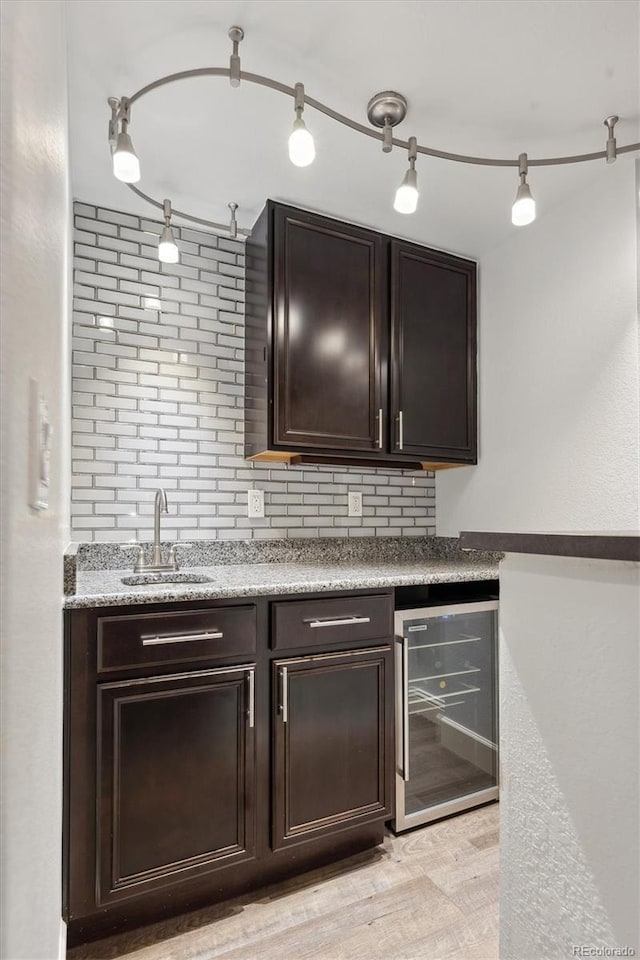 bar featuring backsplash, sink, light hardwood / wood-style flooring, dark brown cabinets, and beverage cooler