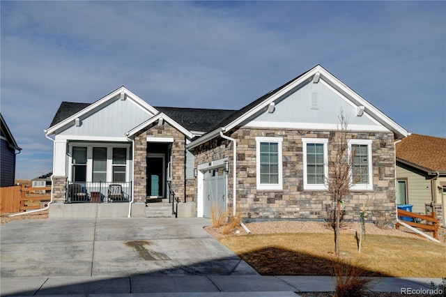 view of front of property with driveway, stone siding, a garage, fence, and covered porch