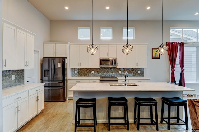 kitchen featuring a sink, light wood-type flooring, appliances with stainless steel finishes, white cabinetry, and light stone counters