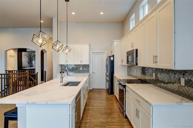 kitchen with a kitchen bar, white cabinetry, a kitchen island with sink, a sink, and stainless steel appliances