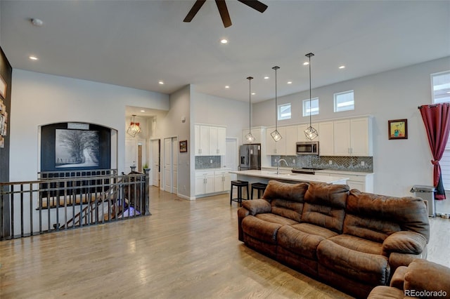 living area with light wood-type flooring, a towering ceiling, a ceiling fan, and recessed lighting