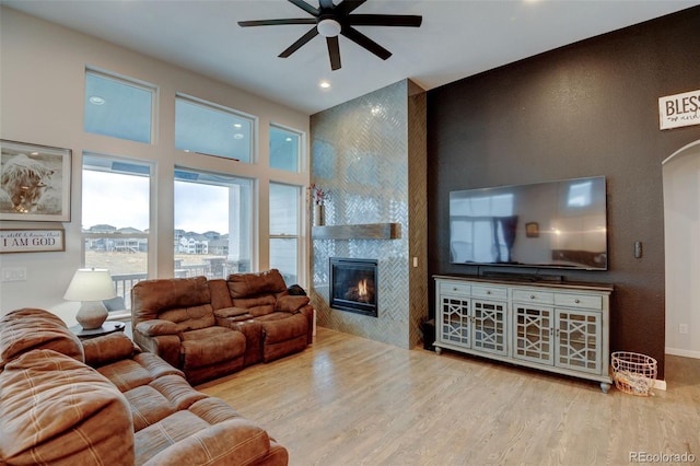 living area with arched walkways, a tile fireplace, wood finished floors, and a ceiling fan