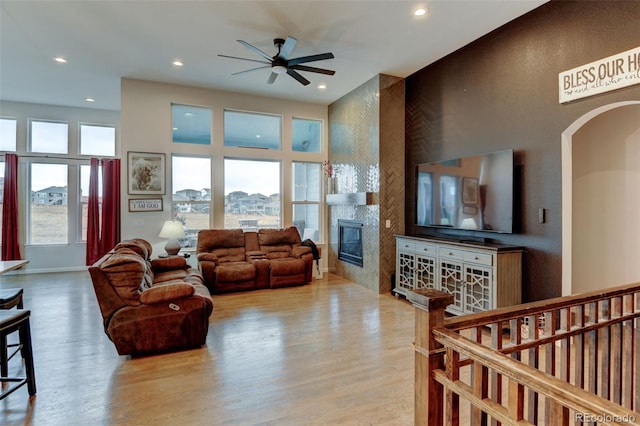 living area featuring arched walkways, a ceiling fan, wood finished floors, a tile fireplace, and plenty of natural light