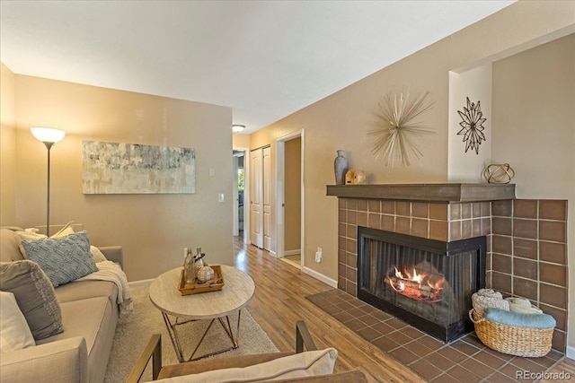 living area featuring baseboards, wood finished floors, and a tiled fireplace