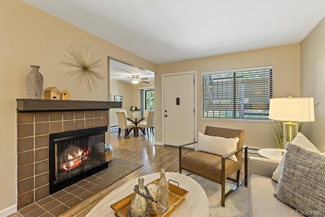 living area featuring baseboards, wood finished floors, and a tiled fireplace