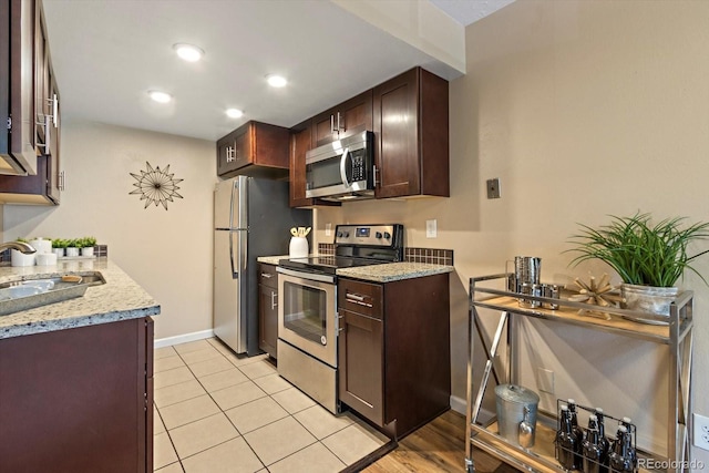 kitchen with light stone counters, dark brown cabinetry, appliances with stainless steel finishes, and a sink