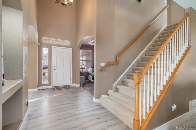 entrance foyer featuring baseboards, stairway, a towering ceiling, wood finished floors, and arched walkways