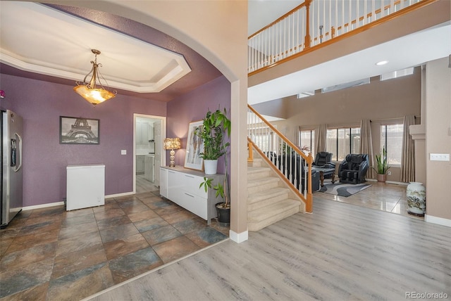 foyer entrance featuring baseboards, stairway, a tray ceiling, wood finished floors, and arched walkways