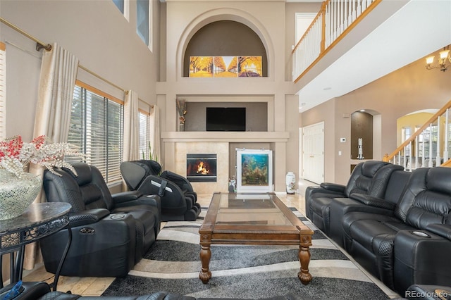 living area with arched walkways, stairway, a tiled fireplace, and an inviting chandelier