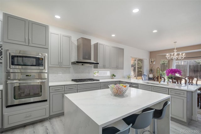 kitchen with gray cabinetry, a peninsula, stainless steel appliances, wall chimney exhaust hood, and a sink