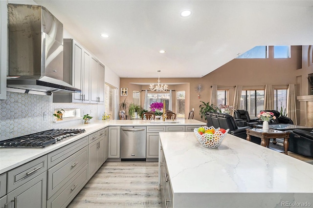 kitchen with gray cabinets, open floor plan, stainless steel appliances, an inviting chandelier, and wall chimney exhaust hood