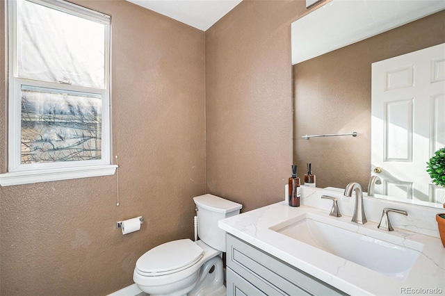 bathroom with toilet, vanity, and a textured wall