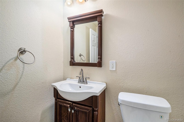 bathroom featuring toilet, vanity, and a textured wall