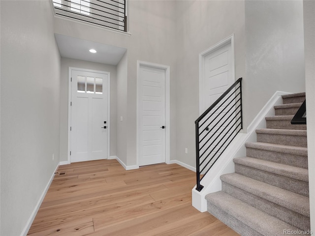 foyer entrance with light wood-style floors, baseboards, a towering ceiling, and stairway