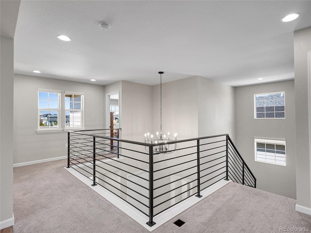 hall with carpet flooring, baseboards, an upstairs landing, and an inviting chandelier