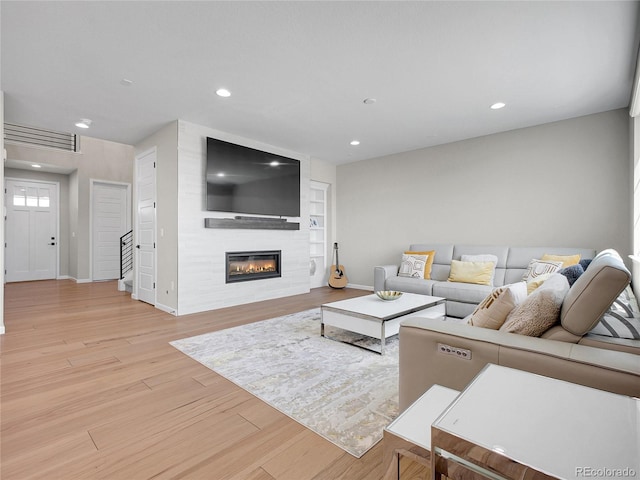 living room featuring stairs, light wood-style floors, baseboards, recessed lighting, and a large fireplace