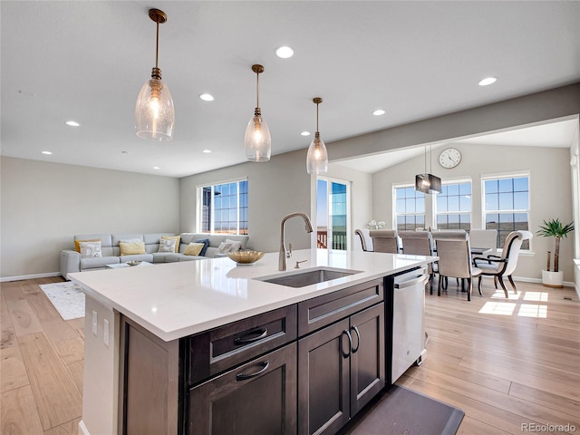 kitchen featuring a sink, light countertops, light wood-type flooring, stainless steel dishwasher, and pendant lighting