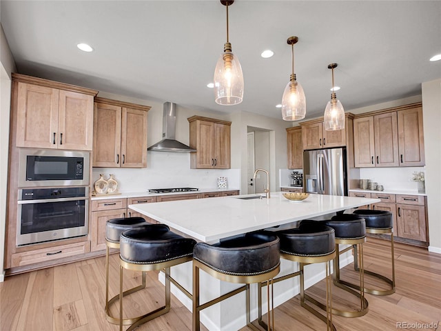kitchen with wall chimney range hood, appliances with stainless steel finishes, a sink, a breakfast bar area, and recessed lighting