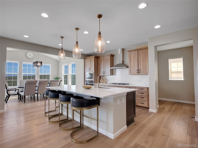 kitchen featuring wall chimney range hood, a sink, light countertops, stainless steel appliances, and a center island with sink