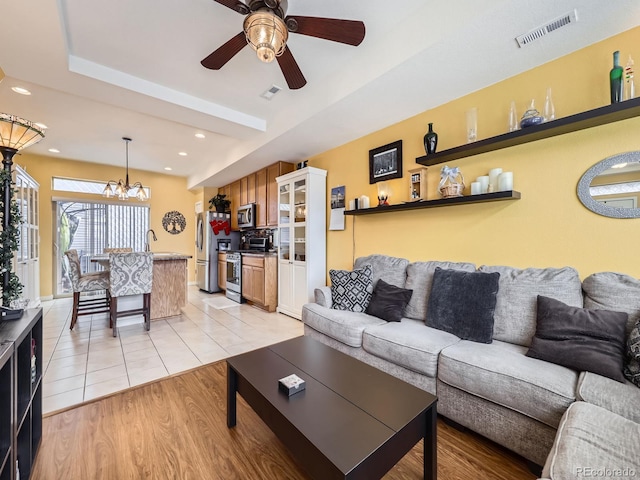 living room with light wood-type flooring and ceiling fan with notable chandelier