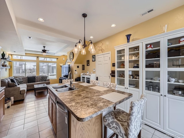 kitchen featuring a kitchen island with sink, sink, stainless steel dishwasher, light tile patterned floors, and a kitchen bar