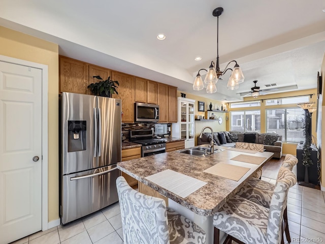 kitchen with appliances with stainless steel finishes, decorative light fixtures, light tile patterned floors, sink, and a kitchen bar