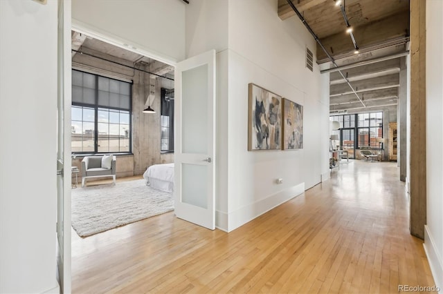 corridor with visible vents, rail lighting, baseboards, a high ceiling, and hardwood / wood-style floors