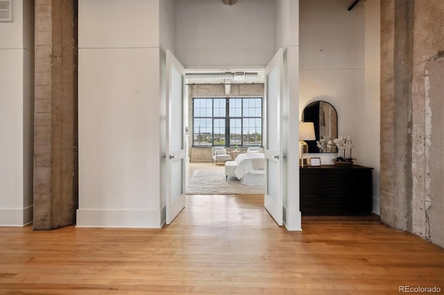 corridor featuring light wood-style floors and a towering ceiling