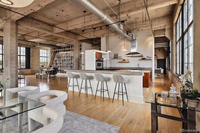 kitchen featuring a breakfast bar, oven, light wood-style floors, a high ceiling, and wall chimney exhaust hood