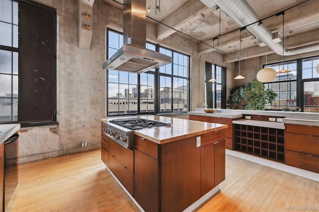 kitchen with island exhaust hood, brown cabinetry, light wood-style flooring, and stainless steel gas cooktop
