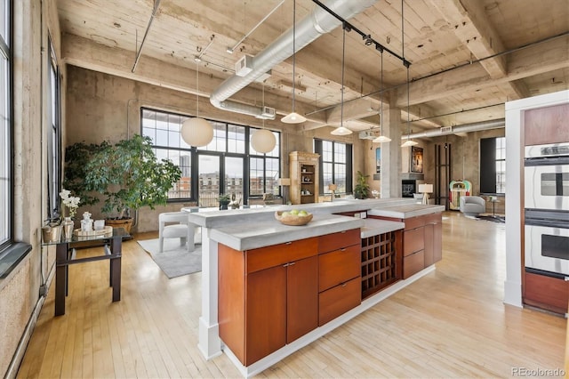 kitchen with stainless steel double oven, brown cabinets, light countertops, light wood finished floors, and open floor plan
