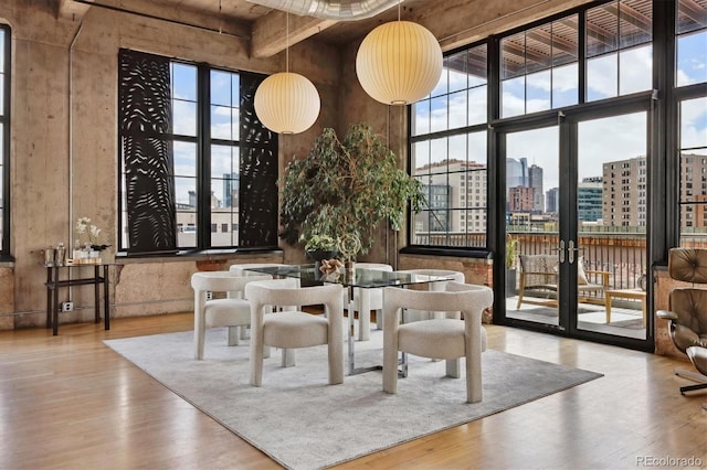 dining space with a view of city, a towering ceiling, wood finished floors, and a healthy amount of sunlight