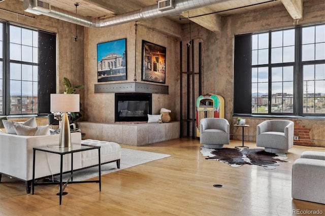 living area with visible vents, a glass covered fireplace, wood finished floors, and a wealth of natural light