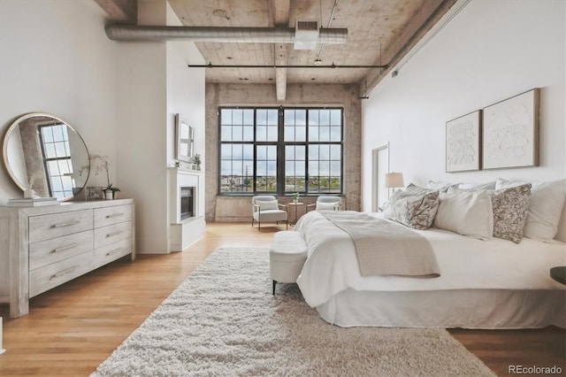 bedroom featuring a glass covered fireplace, a towering ceiling, light wood-type flooring, and visible vents