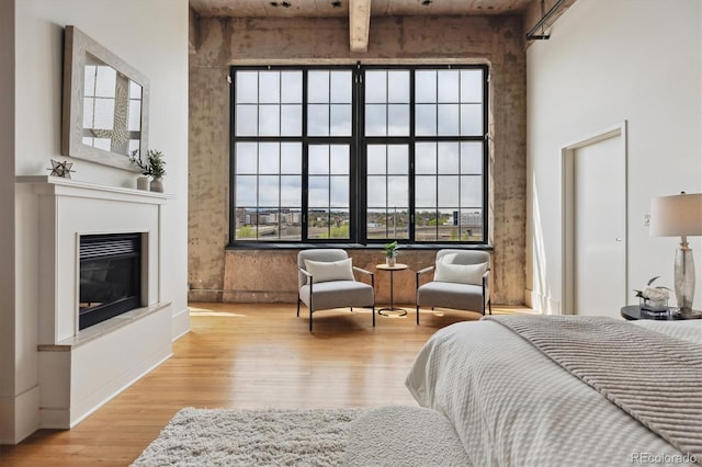 bedroom featuring wood finished floors, a glass covered fireplace, and a high ceiling