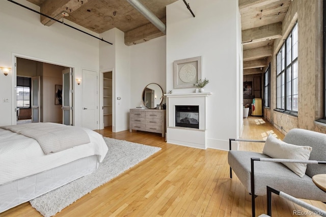 bedroom featuring a multi sided fireplace, a high ceiling, a spacious closet, and light wood-type flooring