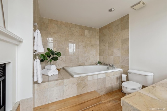 bathroom with a garden tub, visible vents, toilet, tile walls, and hardwood / wood-style flooring