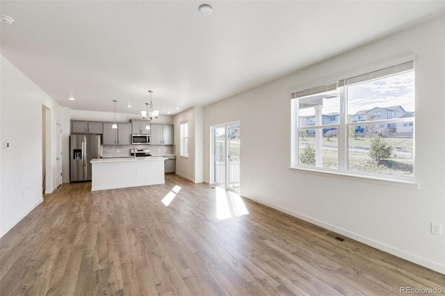 unfurnished living room with an inviting chandelier, sink, and light hardwood / wood-style floors