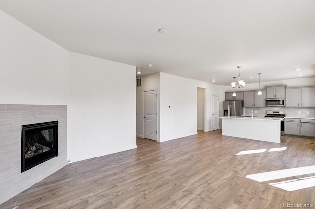 unfurnished living room with a notable chandelier, a tile fireplace, sink, and light wood-type flooring