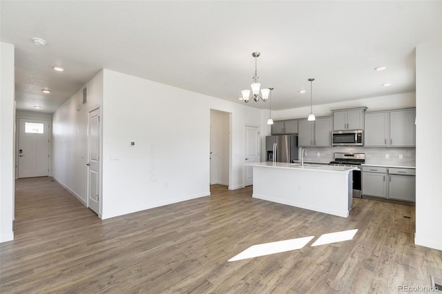 kitchen featuring decorative light fixtures, light wood-type flooring, appliances with stainless steel finishes, gray cabinets, and a kitchen island with sink