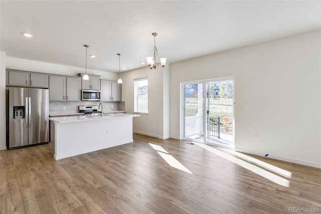 kitchen with tasteful backsplash, decorative light fixtures, appliances with stainless steel finishes, gray cabinets, and an island with sink