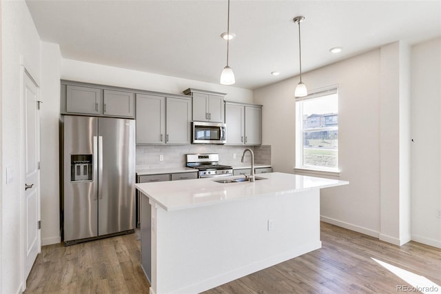 kitchen with an island with sink, stainless steel appliances, sink, and gray cabinetry