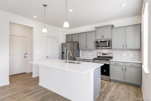 kitchen featuring stainless steel appliances, an island with sink, and gray cabinetry